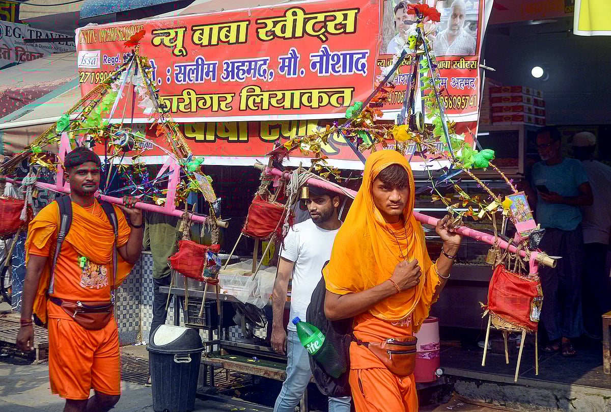 Kanwariyas walk past a shop on which banners with shopkeeper's name was put up on Kanwar Marg after an order issued by Uttar Pradesh Government, in Muzaffarnagar, Saturday, July 20, 2024.  - PTI